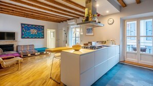 A modern living room with a wooden ceiling, a sofa, a TV, and a kitchen area with a central island. - Easylife - Splendid penthouse in Porta Venezia (Milano)