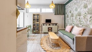 A living room with a sofa, a coffee table, and a television. There is a cabinet with glass doors and a wicker bench.