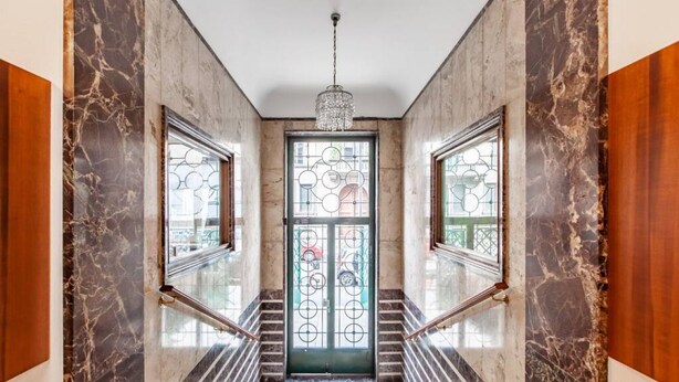 A grand entrance with marble walls, a glass door with circular patterns, and a chandelier.