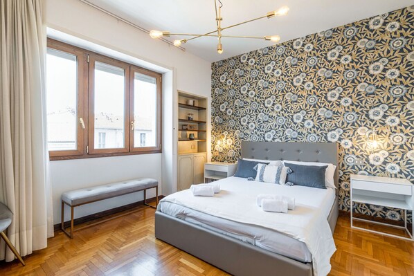 A modern bedroom with a large bed, a bench, a wardrobe, and a patterned wall.