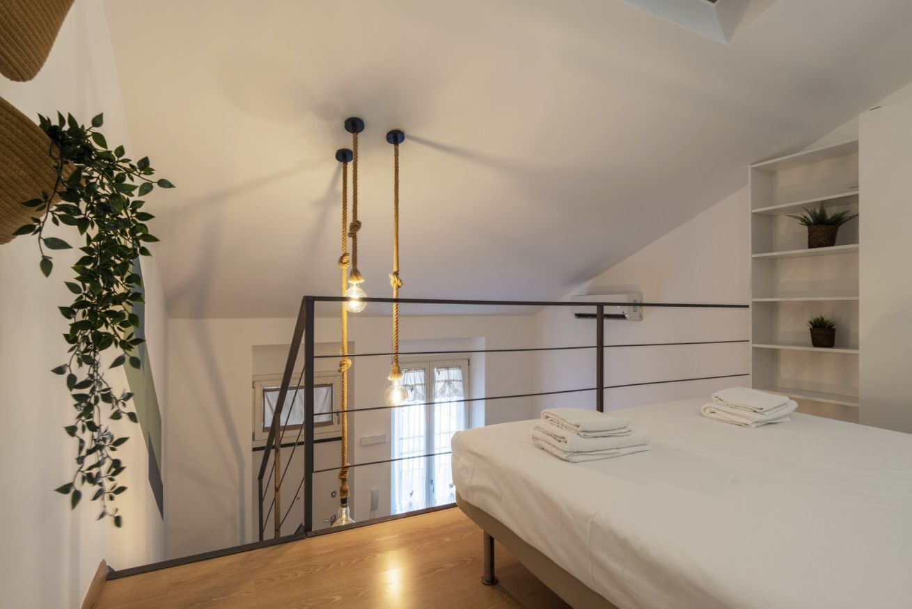 A bedroom with a bed, a staircase, and a shelf with plants.