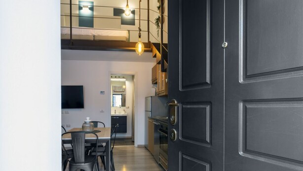 Une cuisine moderne avec des meubles de couleur sombre, un coin repas avec une table et des chaises, et un téléviseur visible au mur.