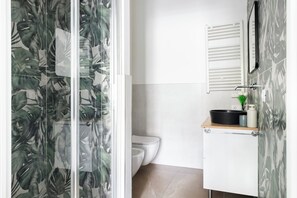 Un baño con inodoro, lavabo con espejo y ducha con puerta de cristal.