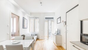 Ein modernes, gut beleuchtetes Zimmer mit Esstisch, Stühlen, einer Couch und einer Küchenzeile.