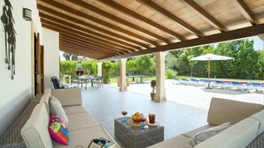 Un espace extérieur aménagé, abrité, avec un canapé en osier, une petite table avec des boissons et un barbecue à l’arrière-plan.