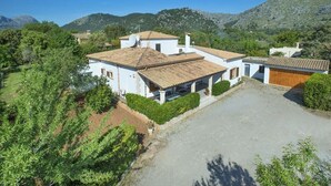 Une villa blanche, dotée d’un toit en tuiles, entourée de verdure et de montagnes.