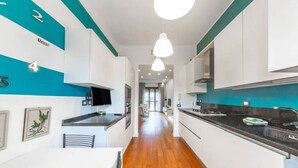 A modern kitchen with white cabinets, a black countertop, and a wooden floor. There are pendant lights, a television, and a framed picture on the wall. - Easylife - Luxurious two-room apartment with balcony and hot tub in the Barona (Milano)