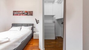 A modern bedroom with a bed, a nightstand, a painting, and a view of a hallway. - Easylife - Luxurious two-room apartment with balcony and hot tub in the Barona (Milano)