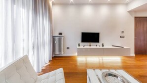 A modern living room with a flat-screen TV, a white entertainment unit, and a wooden floor. - Easylife - Luxurious two-room apartment with balcony and hot tub in the Barona (Milano)