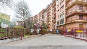 A gated residential complex with multiple apartment buildings, a paved entrance area, and a red metal fence. - Easylife - Luxurious two-room apartment with balcony and hot tub in the Barona (Milano)