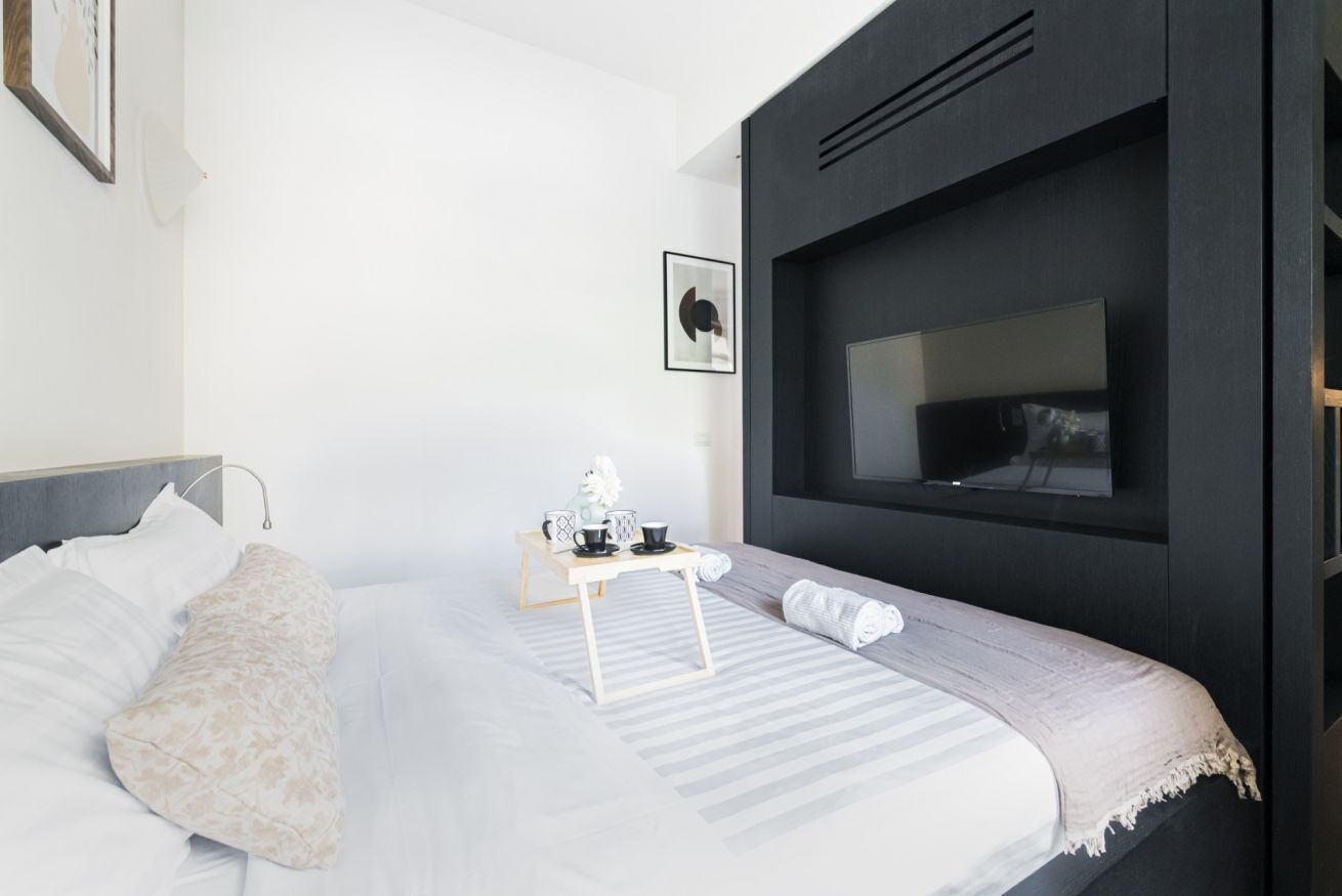Une chambre d’hôtel moderne avec un grand lit, une table de chevet avec une lampe, un tableau encadré au mur et un téléviseur fixé au mur.