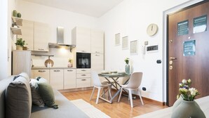 Een moderne keuken met witte kastjes, een eettafel met stoelen, een bank en een vaas met bloemen.