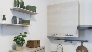 Een moderne keuken met lichte houten kastjes, een roestvrijstalen spoelbak en decoratieve elementen zoals een cactus en gevlochten manden.