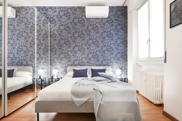 Een slaapkamer met een bed, nachtkastjes, lampen, een radiator en een raam.