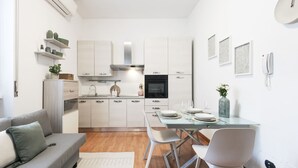 Een moderne keuken met witte kasten, een roestvrijstalen afzuigkap en een eethoek met een glazen tafel en witte stoelen.