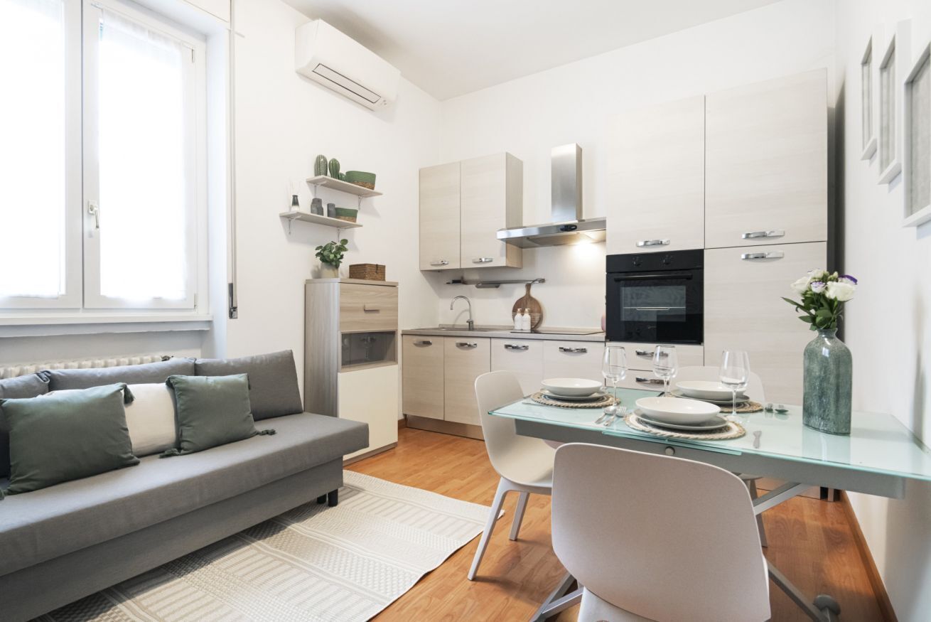 A modern kitchen with white cabinets, a built-in oven, and a dining area with a glass table and chairs.