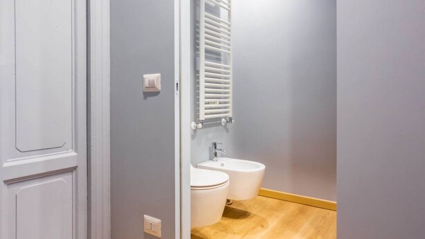 A bathroom with two toilets, a sink, and a towel rack.