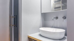 Un baño moderno con cabina de ducha de vidrio, un lavabo blanco y un espejo encima.