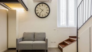 Un salon avec un canapé gris, une horloge murale et un escalier.
