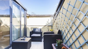 Une terrasse sur le toit avec des sièges extérieurs, une structure vitrée et une clôture en métal.