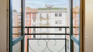 Une vue à travers la fenêtre d’un immeuble d’habitation, avec des balcons, une rambarde en métal et un ciel dégagé.