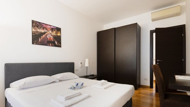 Une chambre d’hôtel avec un grand lit, une armoire sombre, un bureau avec une chaise et un tableau accroché au mur.