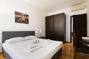 A hotel room with a large bed, a dark wardrobe, a desk with a chair, and a painting on the wall. - Easylife - Elegant apartment in Solari (Milano)