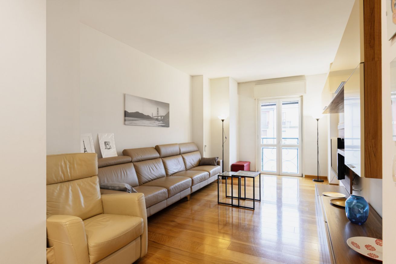 Ein modernes Wohnzimmer mit einem beigefarbenen Ledersofa, einem kleinen schwarzen Couchtisch und Holzböden.
