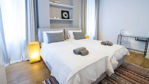 Een moderne slaapkamer met een groot bed, nachtkastjes, een wandplank met boeken en een bedlamp.