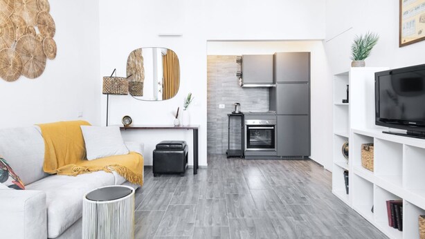 Un salon moderne avec un canapé, une table basse et un téléviseur. Il y a également un coin cuisine équipé d’une cuisinière, d’un four et de placards.