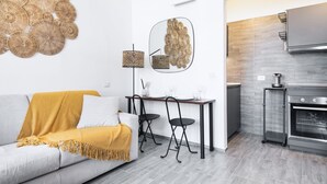 Un salon moderne comprenant un canapé, une table basse et deux fauteuils. Il y a également un coin cuisine avec une cuisinière et un four à micro-ondes.