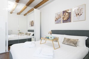 A modern hotel room with a large bed, a bedside table with a vase and a bowl, and a mirror reflecting the room. There are framed botanical prints on the wall. - Easylife - Superb and refined apartment in the Navigli area (Milano)