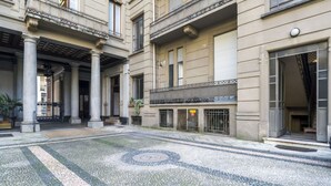Un cortile con pavimento in pietra, colonne e l'ingresso di un edificio con un cartello.