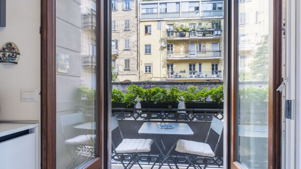Un balcone con tavolo e sedie, affacciato su un edificio con numerosi balconi e piante.