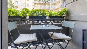 Un balcone esterno con due sedie pieghevoli e un tavolino, con vista su un edificio con balconi e vegetazione.