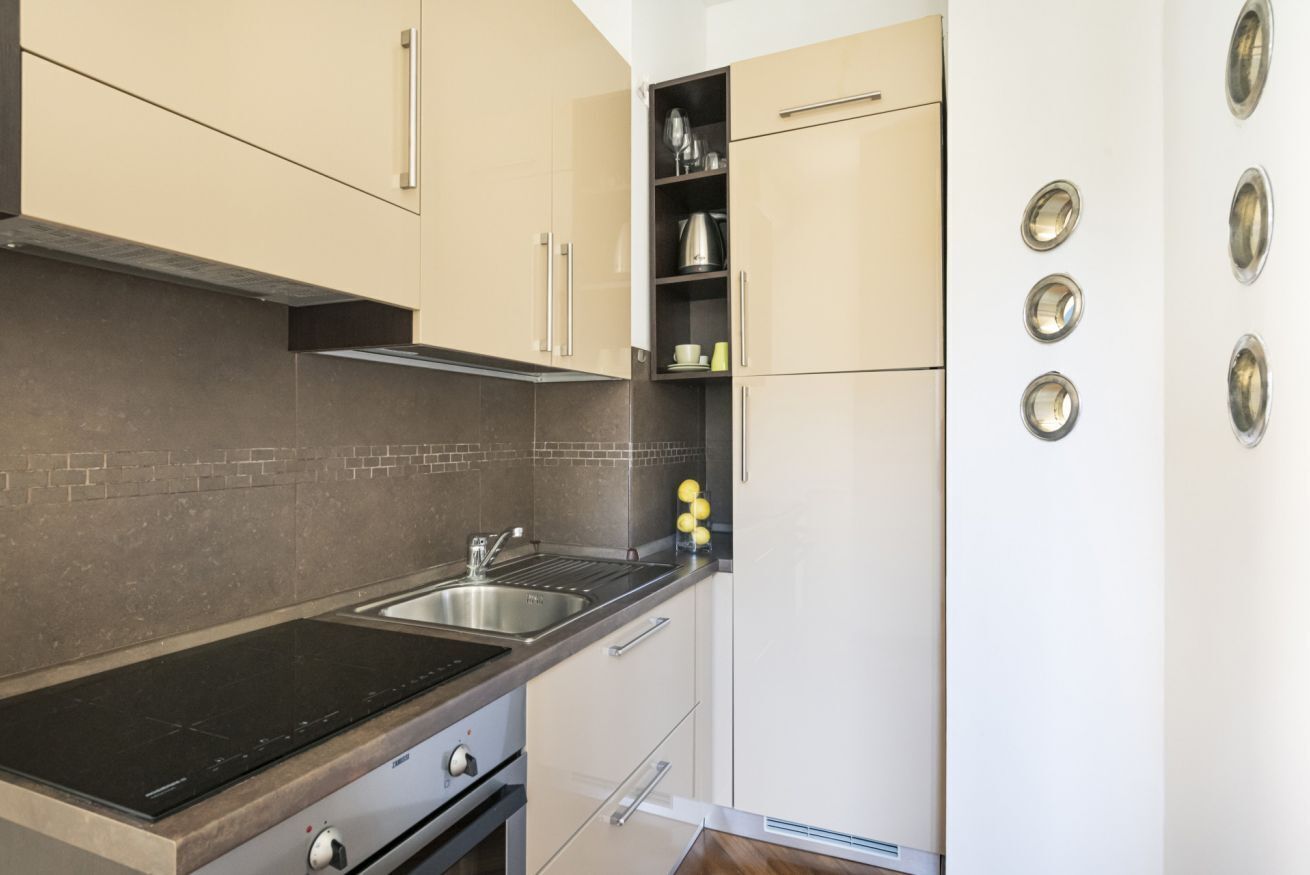 A modern kitchen with a black stovetop, stainless steel sink, and beige cabinetry.