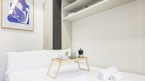 Una habitación de hotel moderna con una cama, una mesita de noche de madera con cafetera y toallas enrolladas.