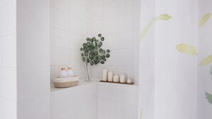 Un baño con azulejos blancos, una planta y artículos de aseo en un estante.