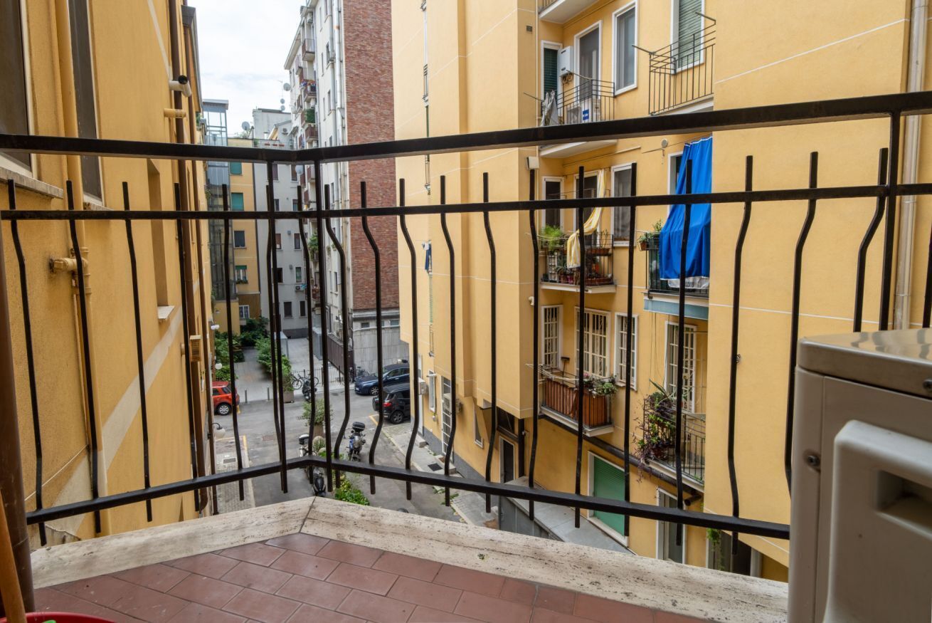 A balcony with a metal railing overlooking a narrow street with yellow buildings.