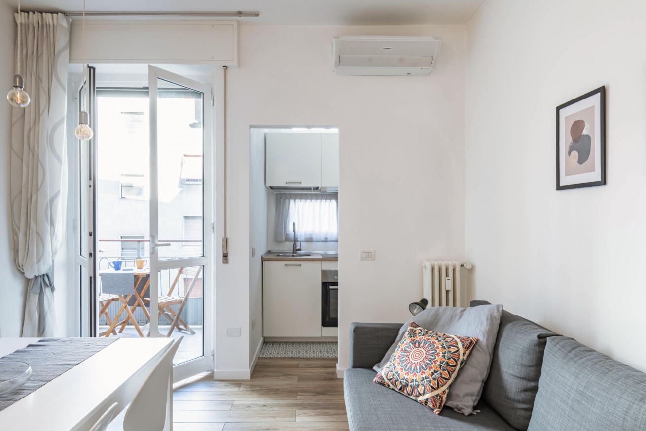 A modern apartment with a dining area, kitchenette, and a living room with a sofa and decorative pillows.