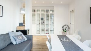 Ein modernes Wohnzimmer mit einem grauen Sofa, einem Esstisch mit weißen Stühlen und einer großen Vitrine mit Regalen.