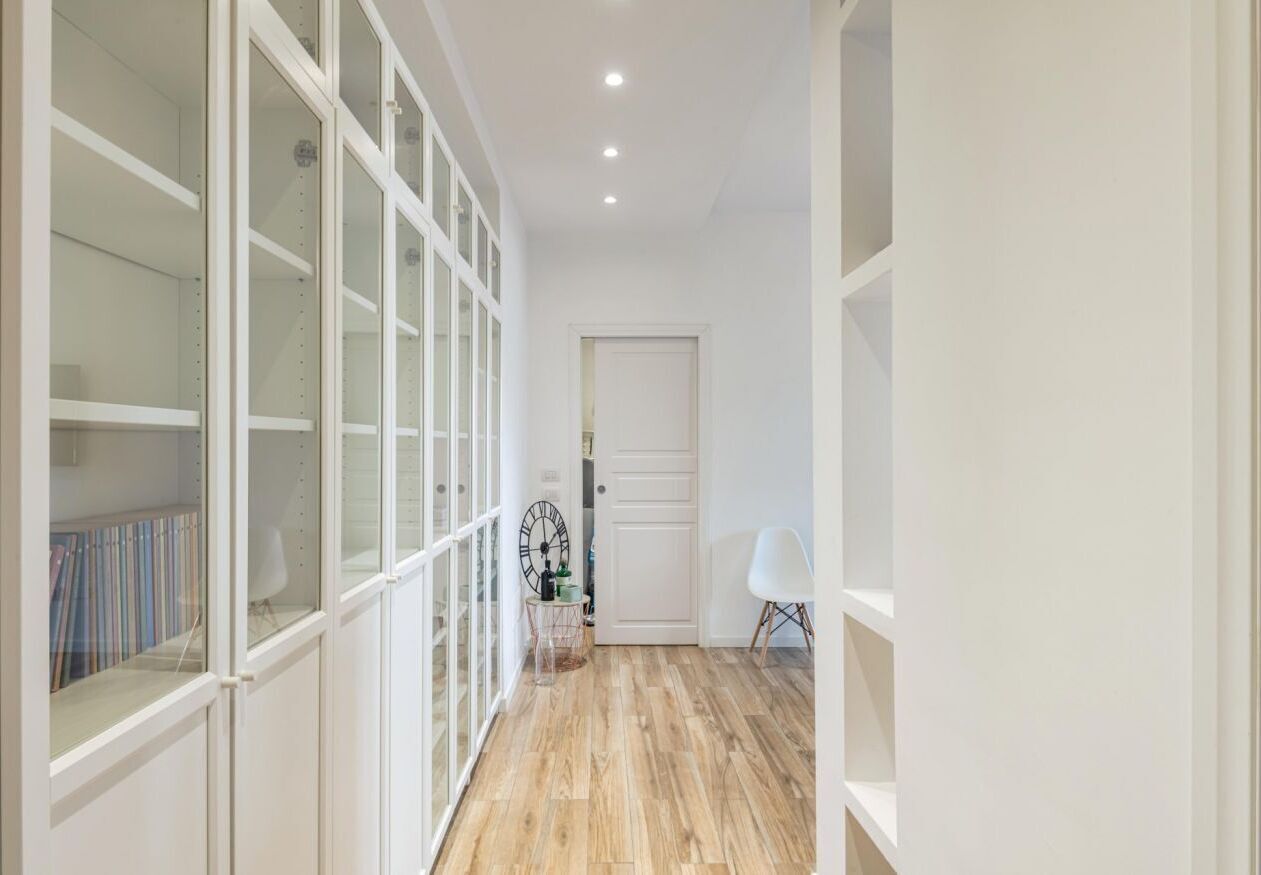 A hallway with white walls, a wooden floor, and a white door at the end.