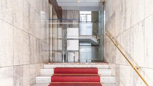 Ein modernes Interieur mit Marmorwänden, einem gläsernen Aufzug und roten Teppichstufen.