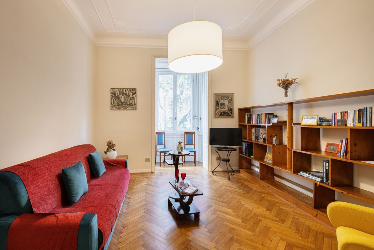 Un salon avec un canapé rouge, des étagères en bois, une table basse et une grande fenêtre.