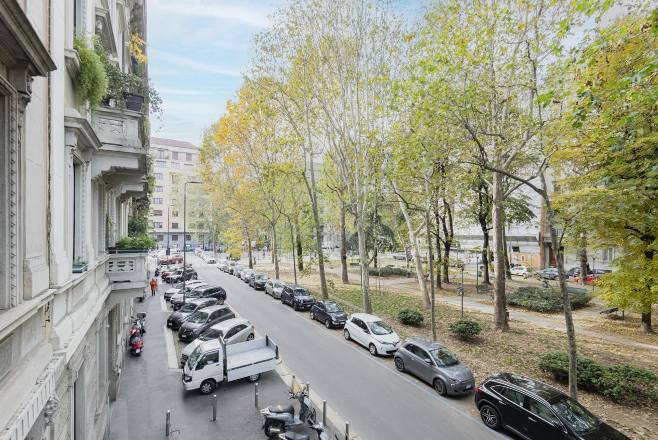 Calle bordeada por vehículos estacionados y árboles, con edificios a un lado.