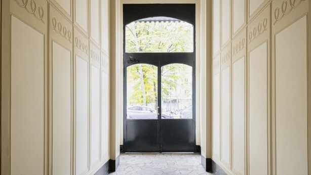 Un couloir avec une porte noire et une vue sur les arbres et les voitures à l’extérieur.