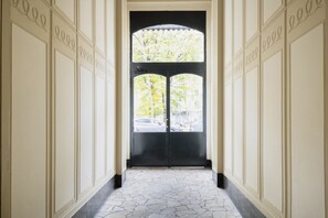 A hallway with a black door and a view of trees and cars outside. - Easylife - Classy gem in Porta Venezia (Milano)