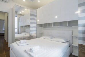 A modern hotel room with a large bed, a mirrored wardrobe, and a built-in shelf.