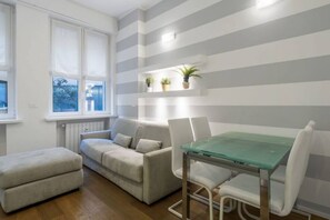 A modern living room with a sofa, ottoman, and a glass-top dining table with chairs.