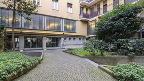 Un patio con senderos de adoquines, un edificio con ventanas amplias y vegetación.